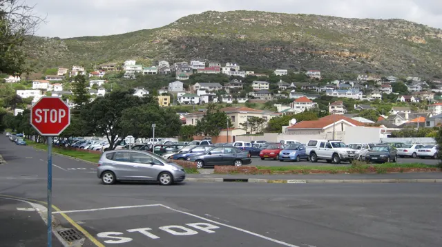 A stop sign faces traffic below houses scattered across a hillside.