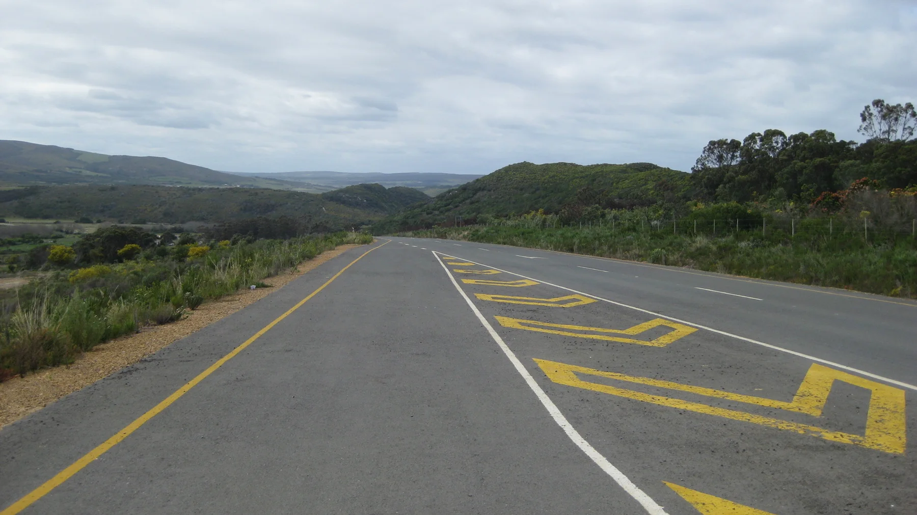Bold yellow markings cross a broad road through open scrubland.