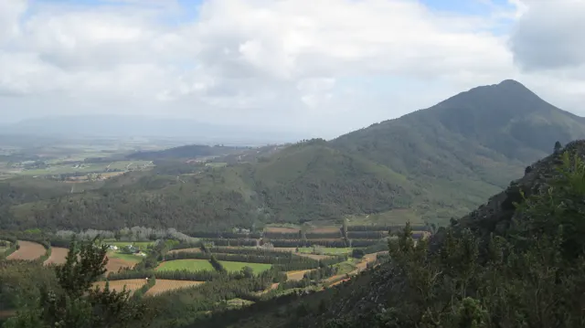 Cultivated fields spread below a long green mountain ridge.