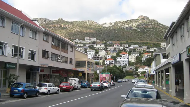 A town street leads toward tightly packed hillside houses.
