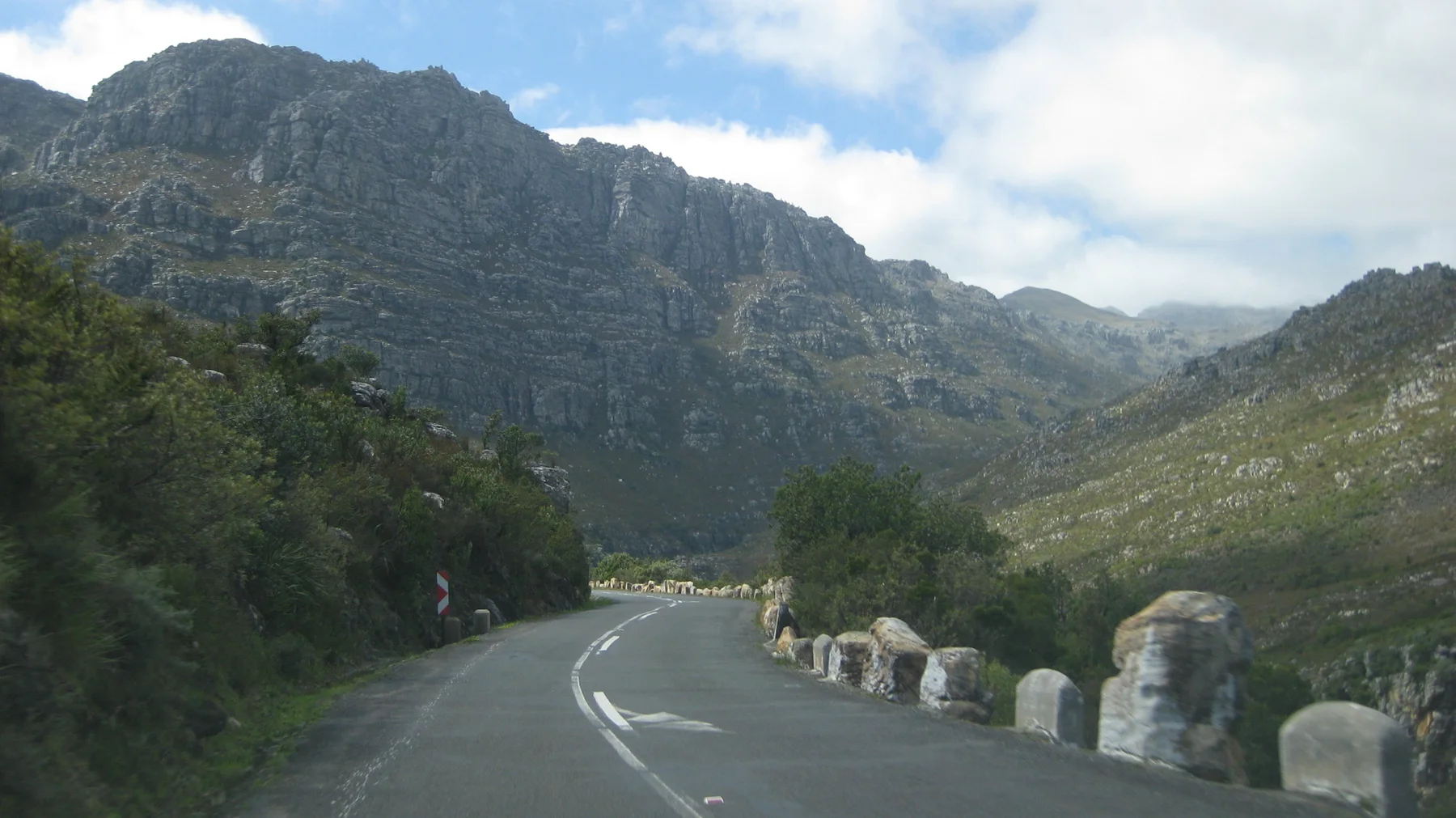 Stone roadside posts follow a bend below steep green mountain walls.