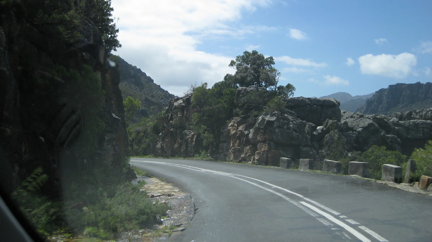 A double-lined road bends between exposed rock and stone roadside posts.