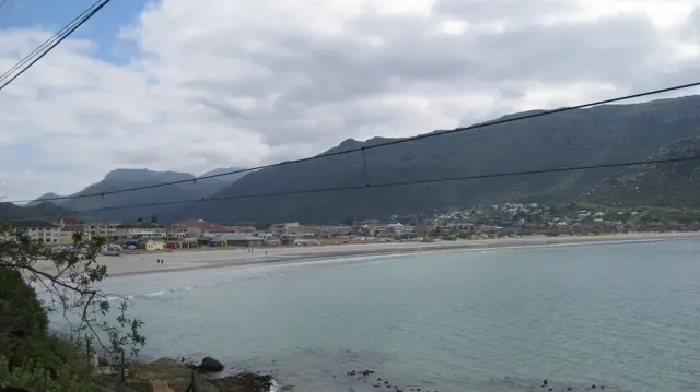 Overhead wires cross a view of coastal buildings and a broad mountain across water.