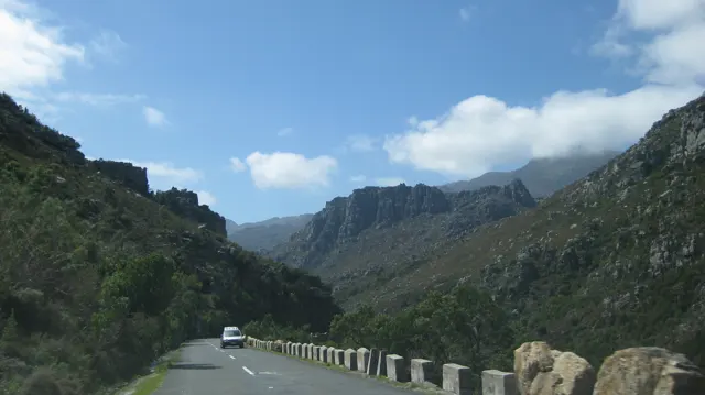 A white vehicle follows a mountain road edged with stone posts.