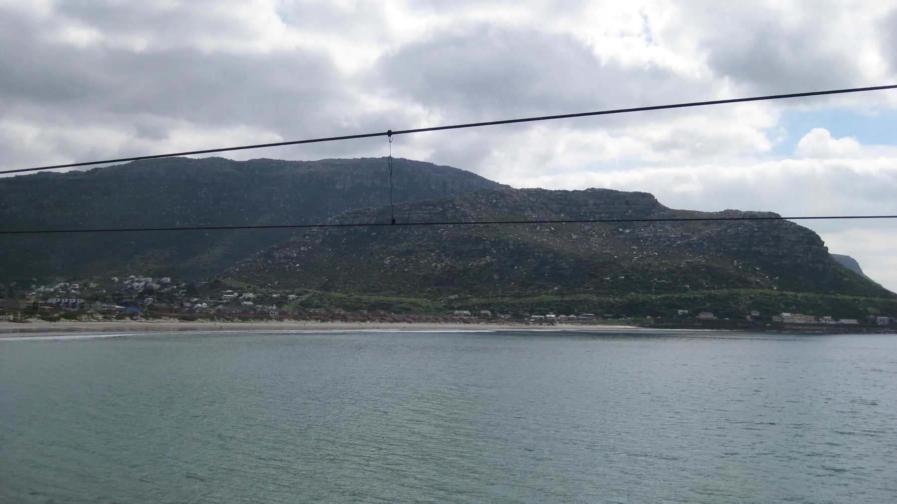 A long mountain rises across calm water beneath overhead wires.