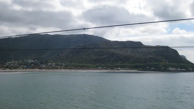 A long mountain rises across calm water beneath overhead wires.