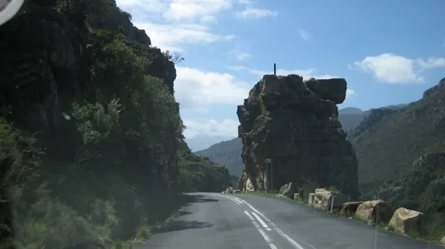 A narrow road passes between towering rock formations and roadside stone posts.