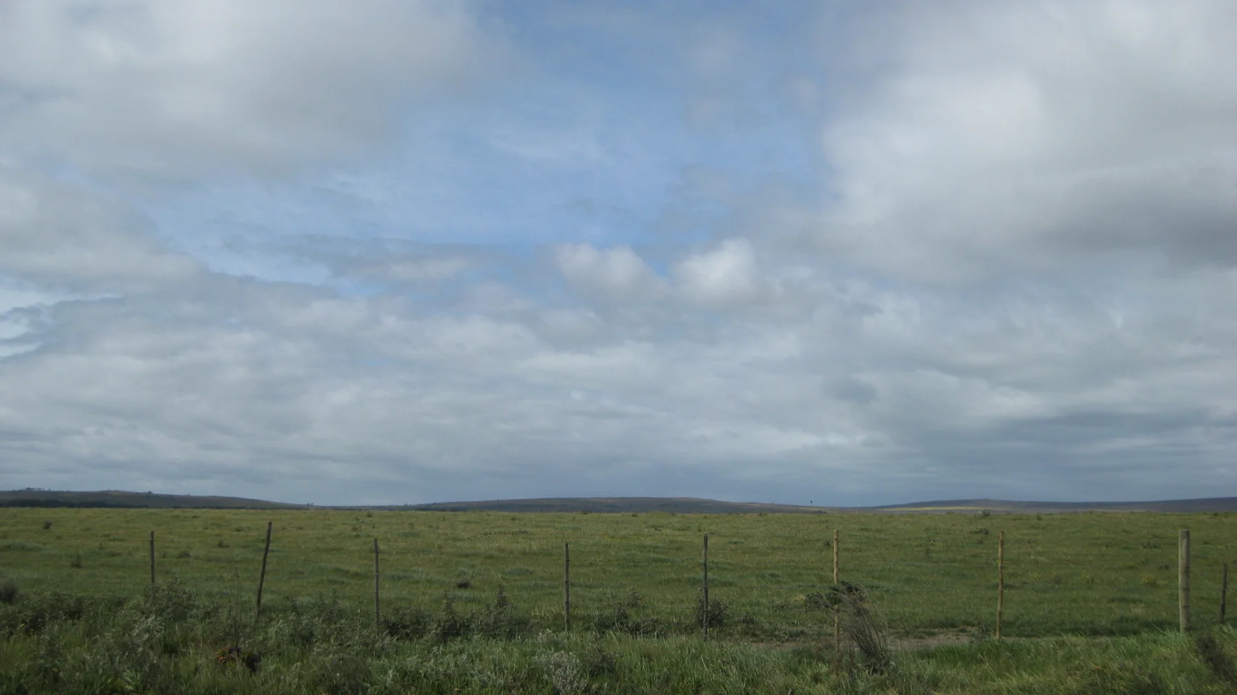 A low fence borders a flat field beneath a wide gray sky.