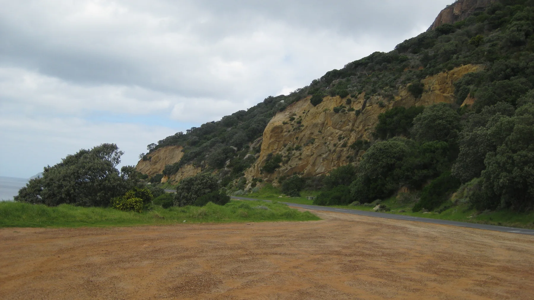 A sandy clearing lies below a steep vegetated cliff.