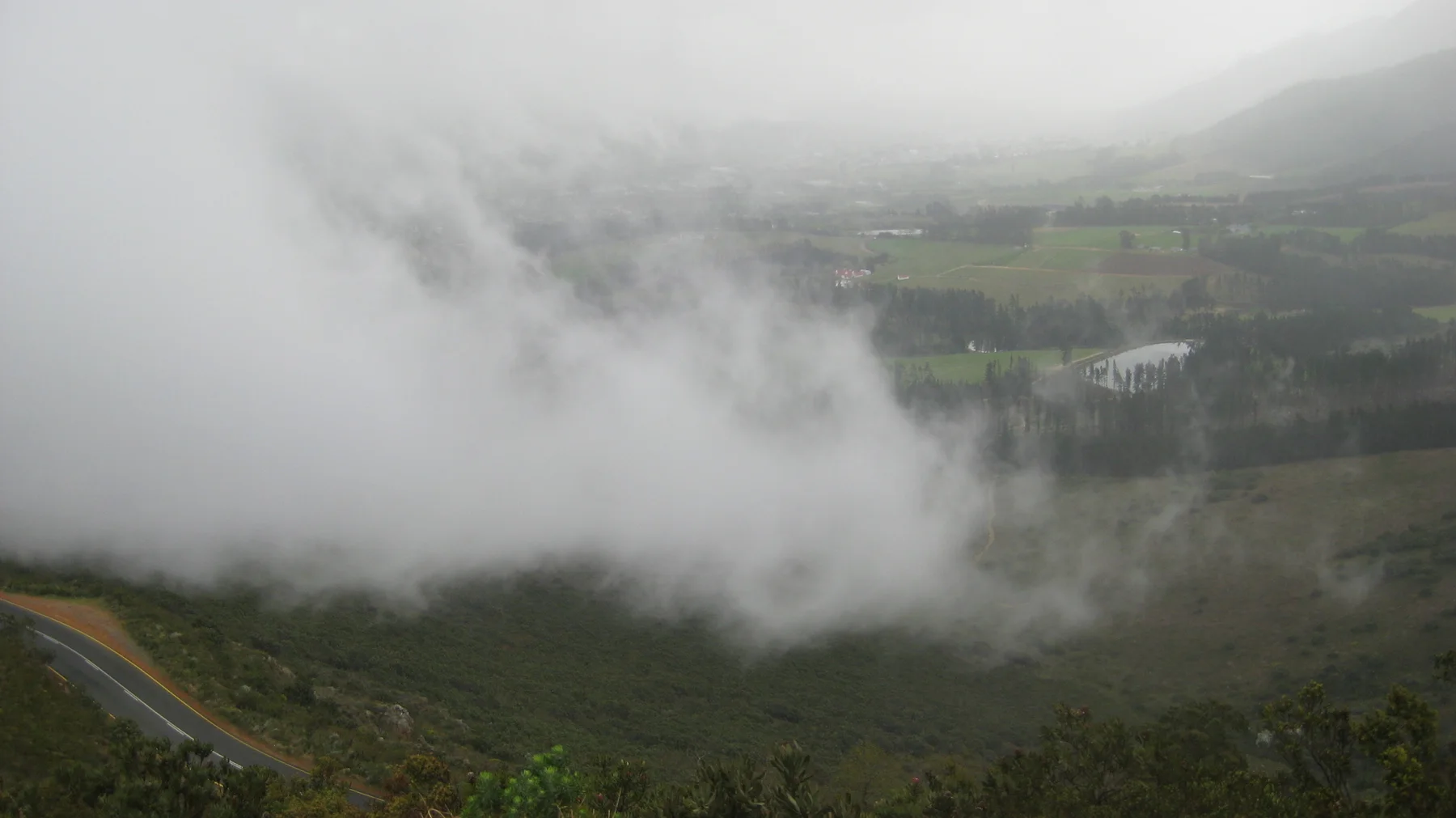 A thick bank of cloud drifts across a steep green valley.