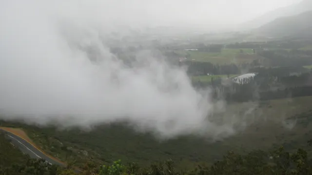 A thick bank of cloud drifts across a steep green valley.