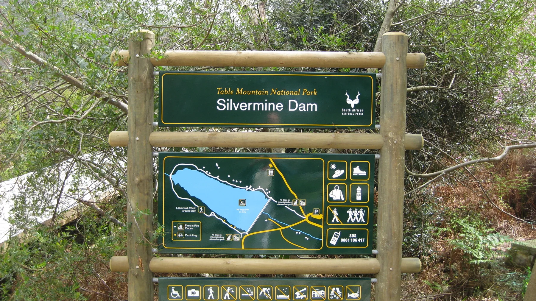 A wooden-framed Silvermine Dam sign displays a map among leafy trees.
