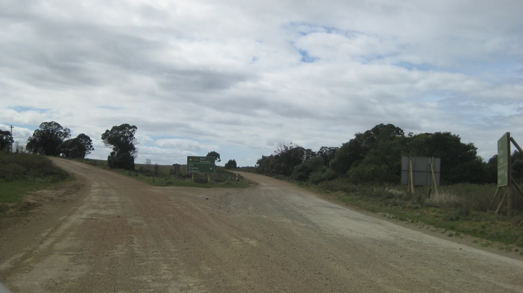 A gravel road forks beside grass and scattered roadside signs.