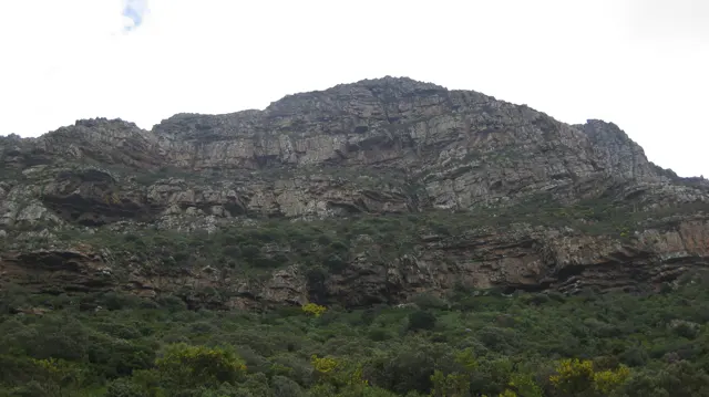 A broad layered rock face rises above dark green vegetation.