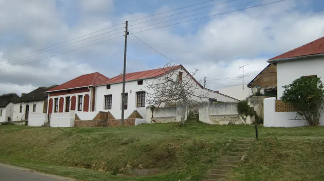 White roadside buildings with red roofs stand behind a grassy verge.