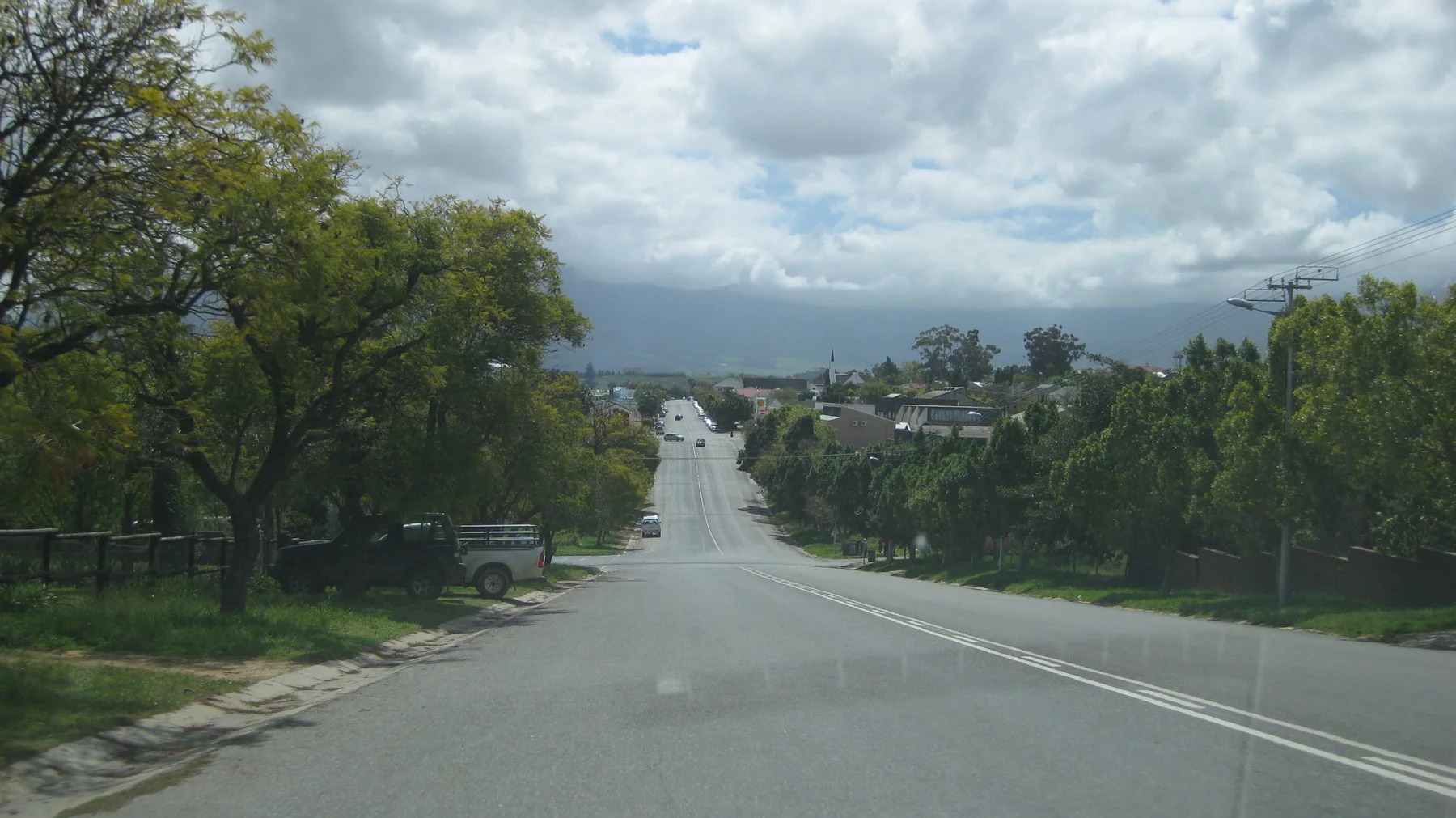 A straight road descends between leafy residential areas toward distant development.