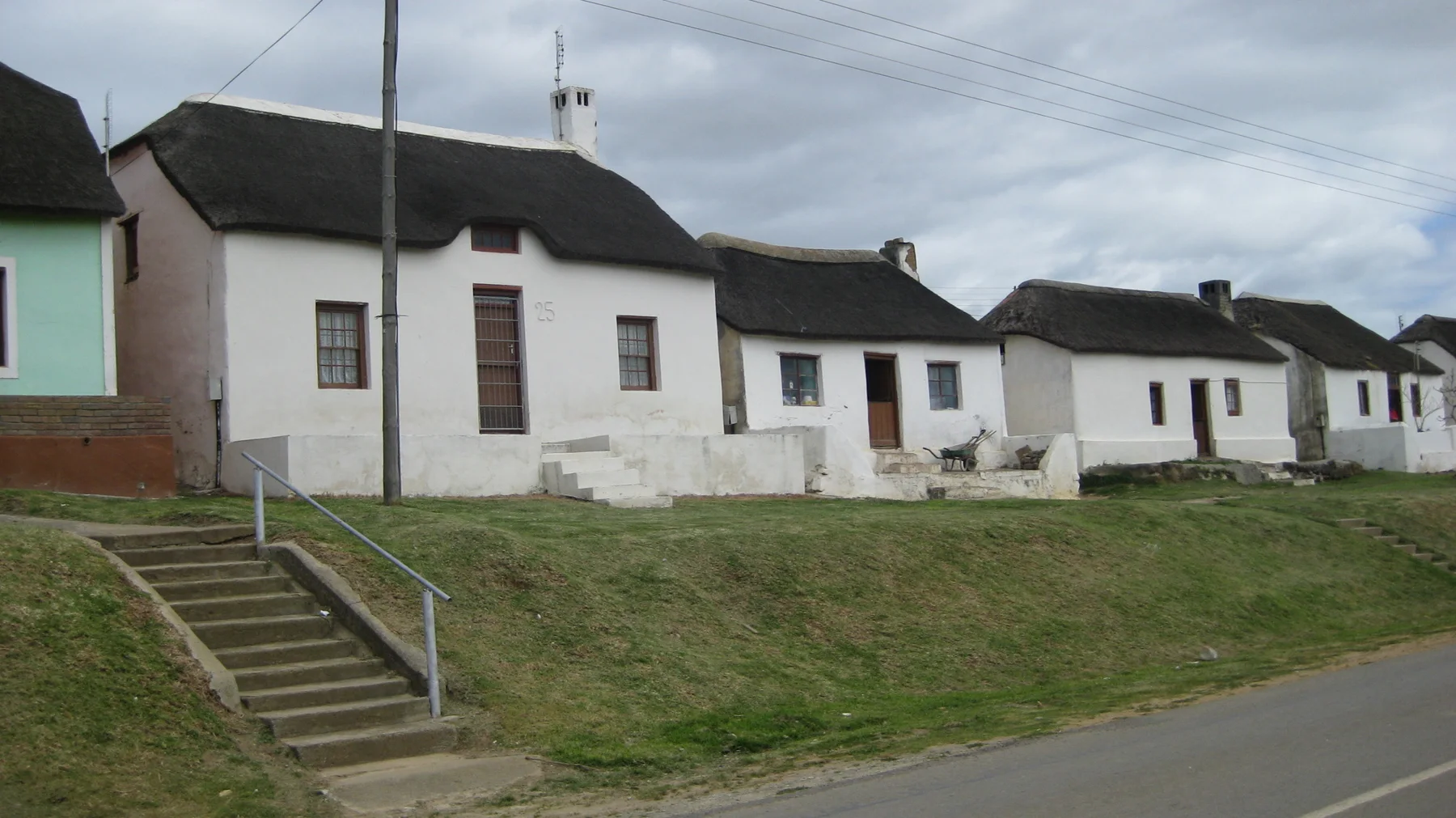 White houses with dark thatched roofs line a grassy roadside slope.