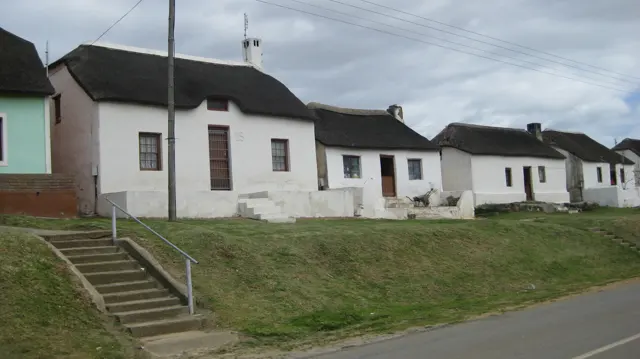 White houses with dark thatched roofs line a grassy roadside slope.