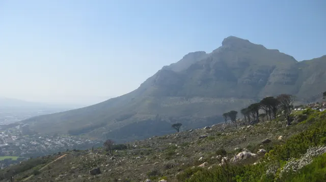 A broad mountain rises above a hazy city and rocky foreground.