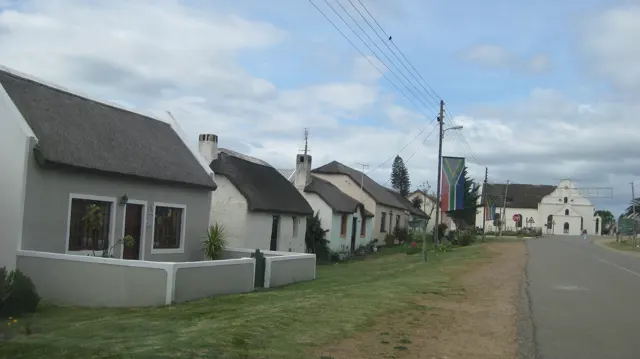 Small pale thatched houses line a quiet village street.