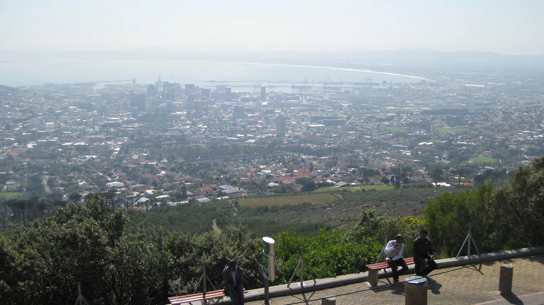 People stand at a lookout above a city stretching toward the sea.