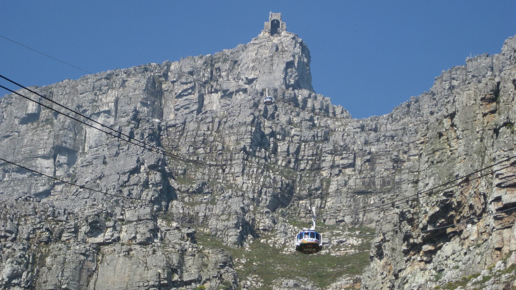 A cable car hangs beneath cables against a sheer rock face.