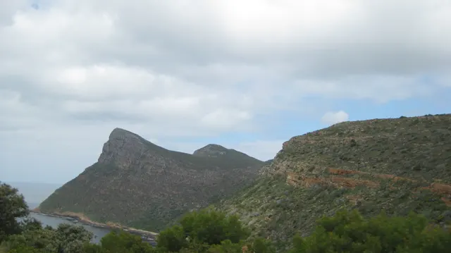 A sharply angled coastal peak rises beyond green hillside vegetation.