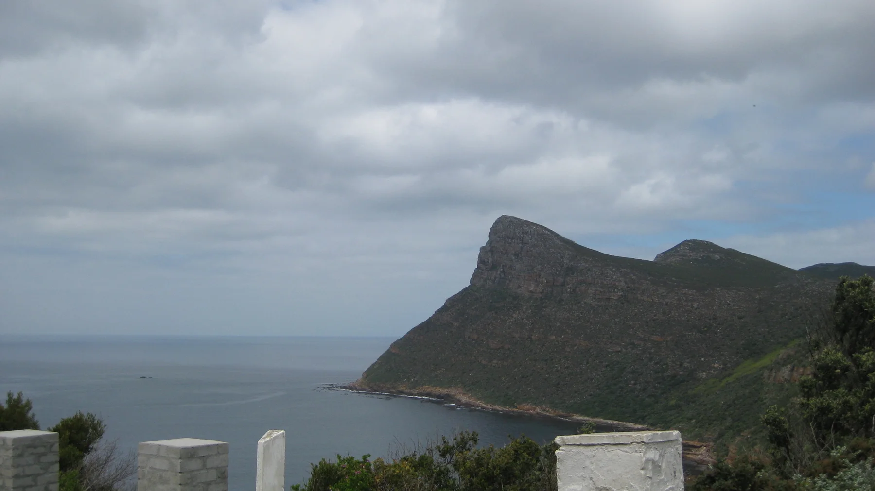White roadside posts frame a view of a steep headland and calm sea.