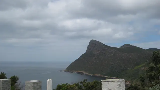 White roadside posts frame a view of a steep headland and calm sea.