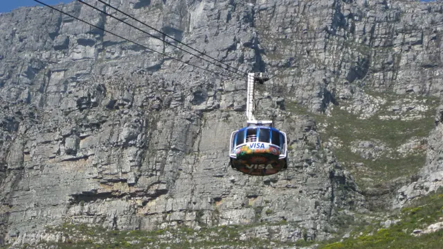 A cable car cabin hangs before a deeply textured rock wall.