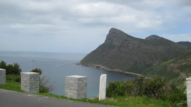 White roadside posts overlook calm water and a rugged coastal peak.