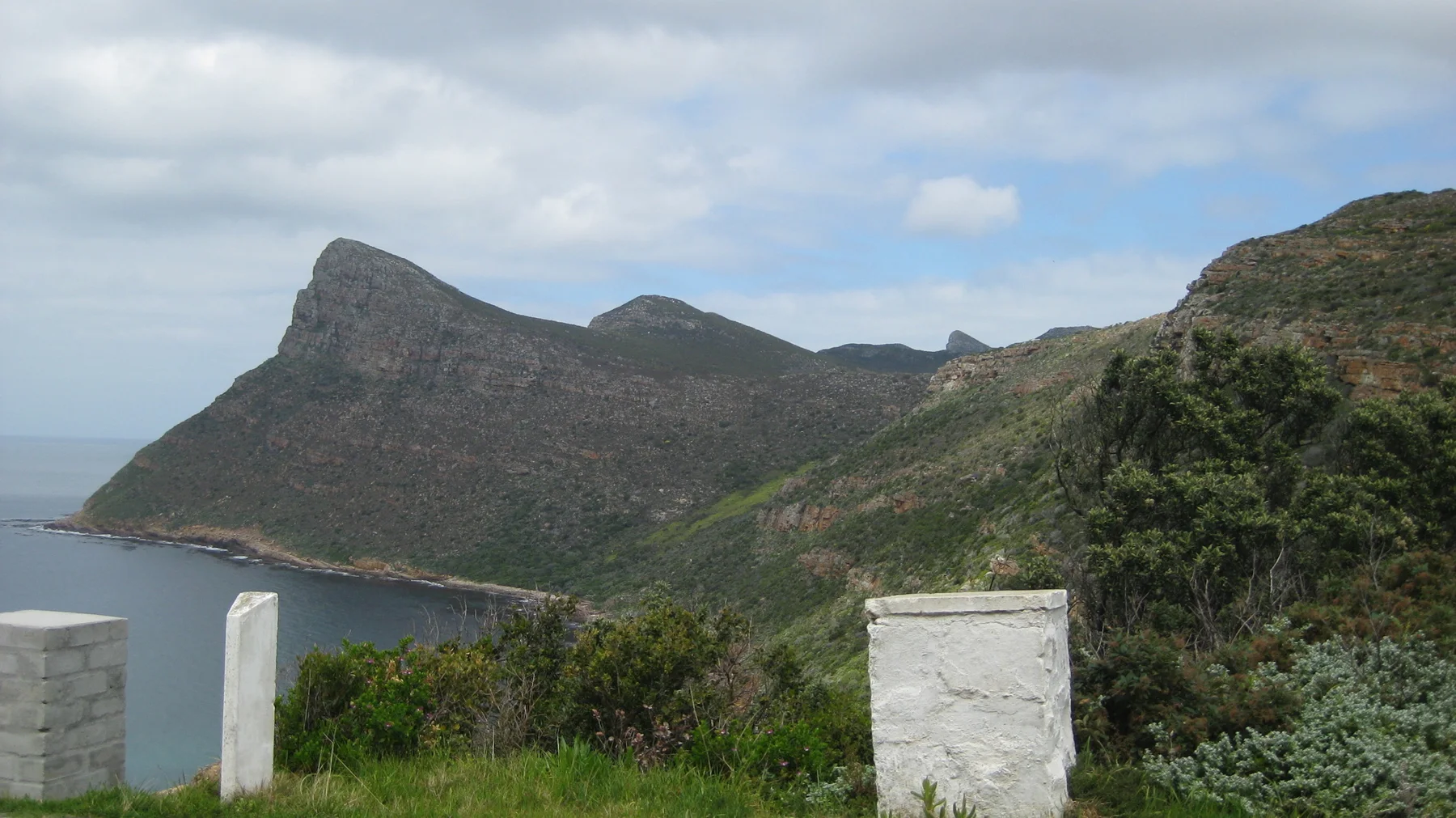 Rocky ridges rise above a quiet bay beyond roadside posts.