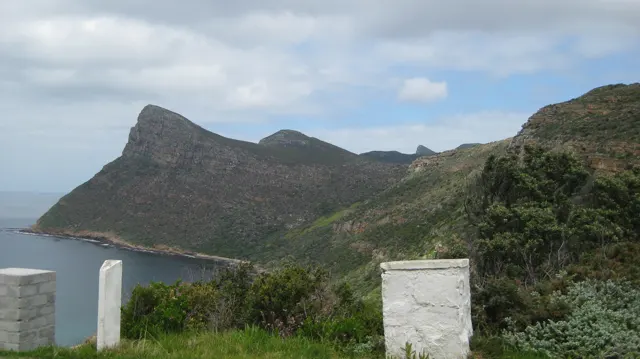 Rocky ridges rise above a quiet bay beyond roadside posts.