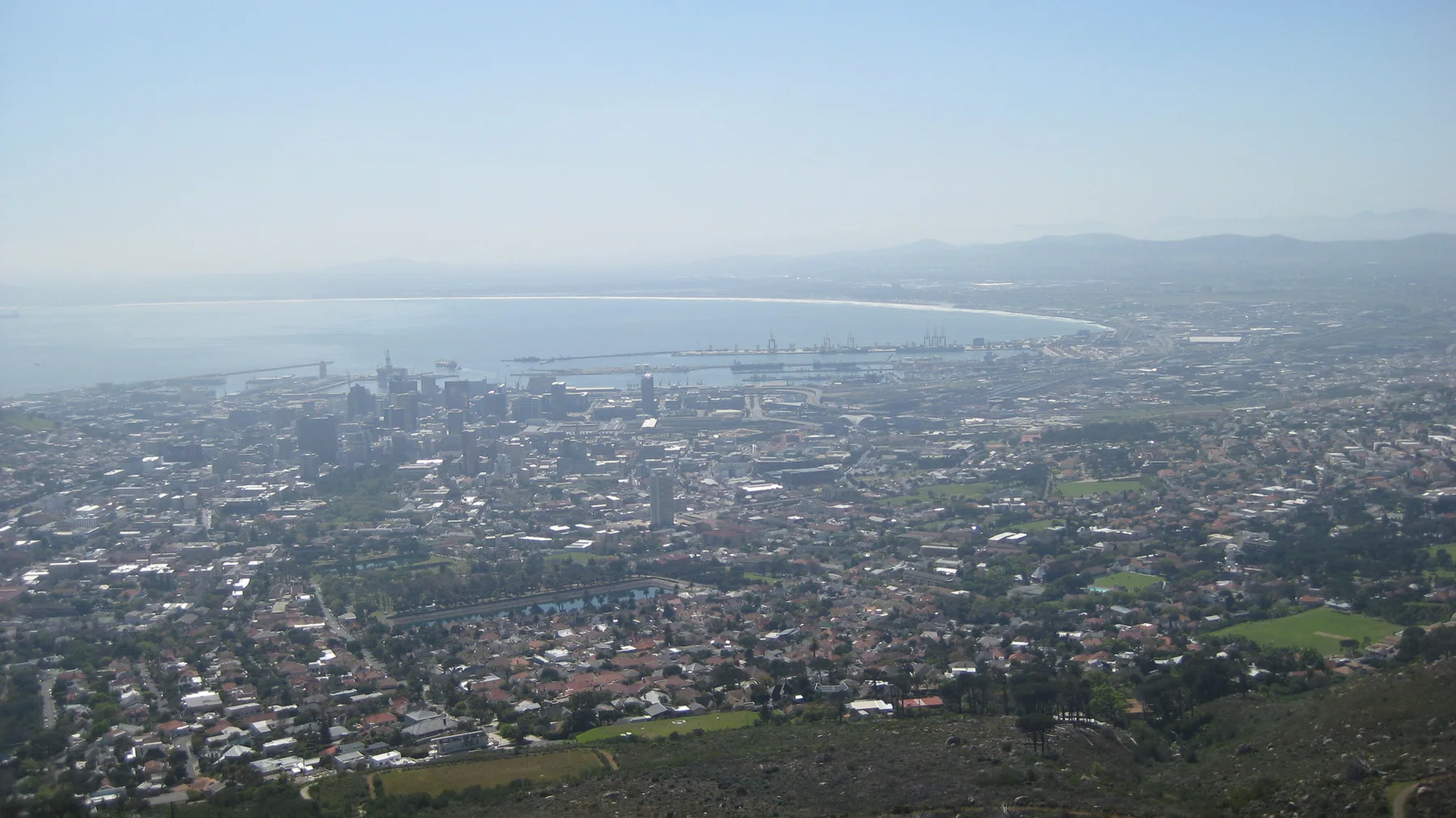 Dense city buildings fade into haze near a pale coastal horizon.
