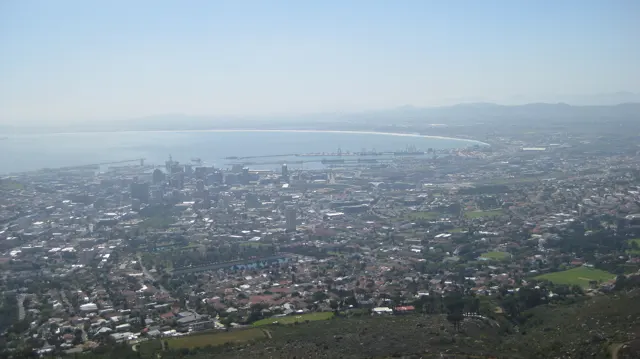 Dense city buildings fade into haze near a pale coastal horizon.