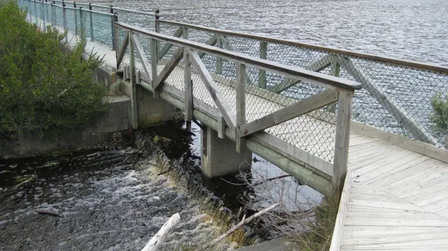 A wooden footbridge with mesh railings crosses a narrow water channel.