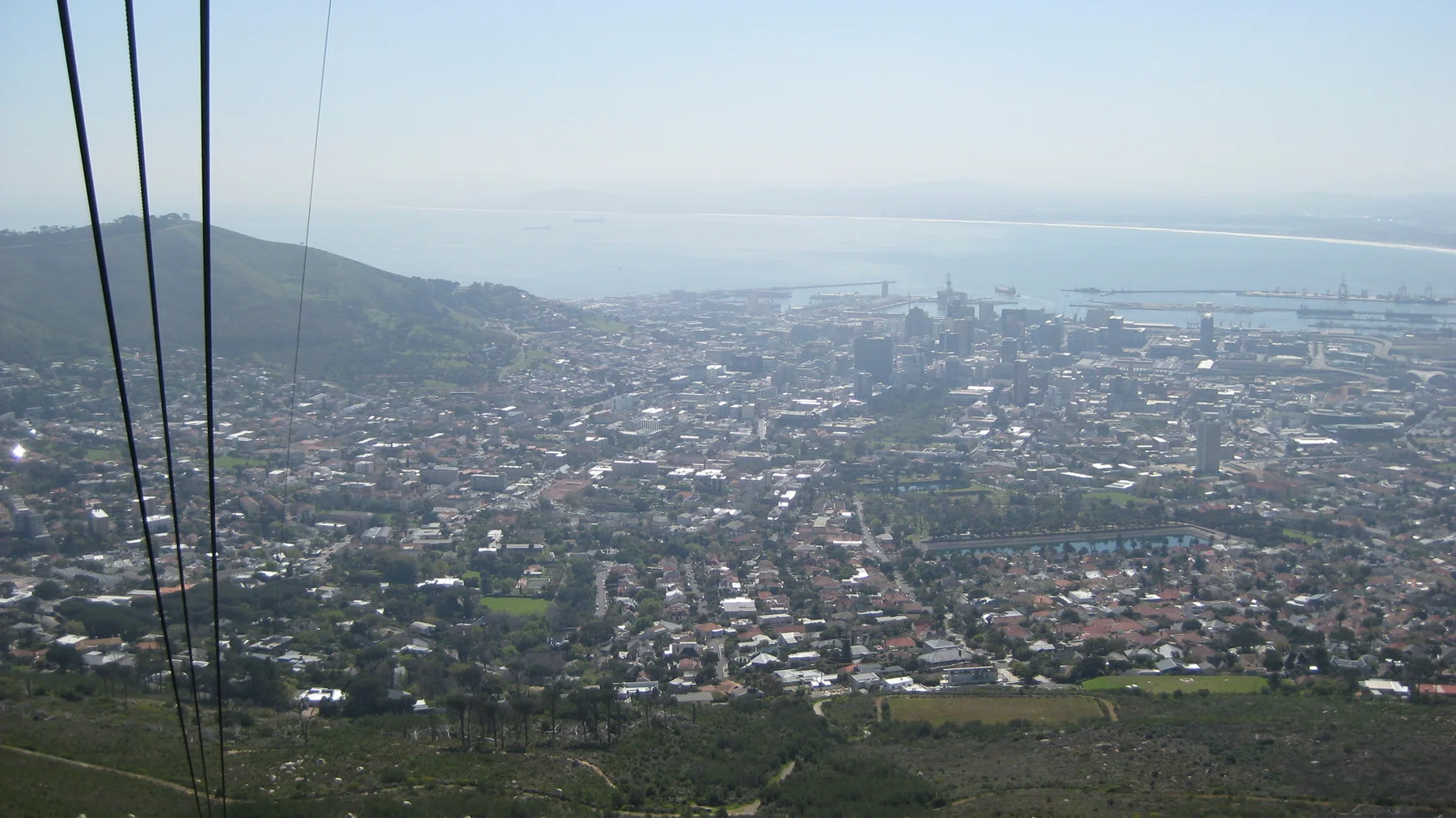 Dark cable lines descend across a high view of city and bay.