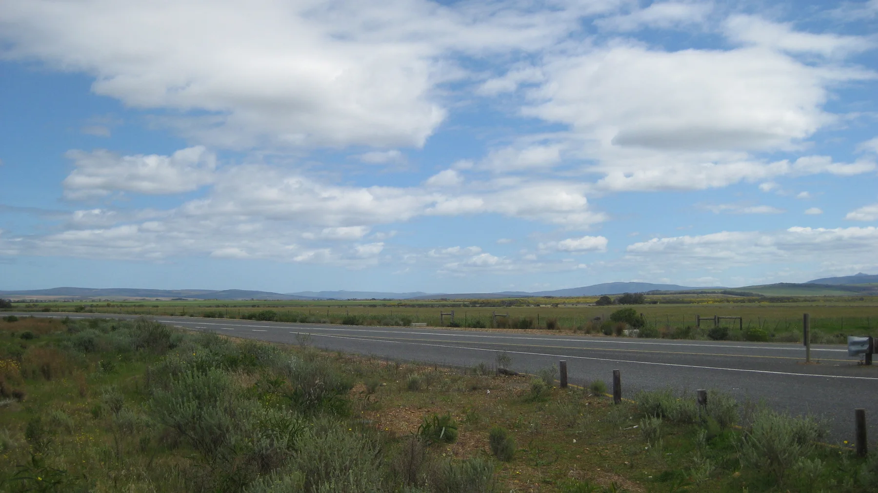 A road crosses open land beneath scattered white clouds.