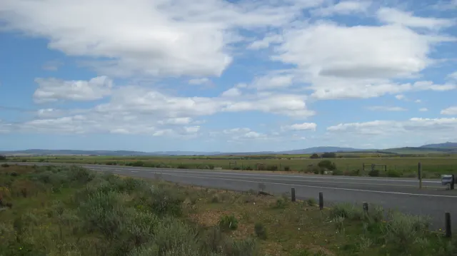 A road crosses open land beneath scattered white clouds.