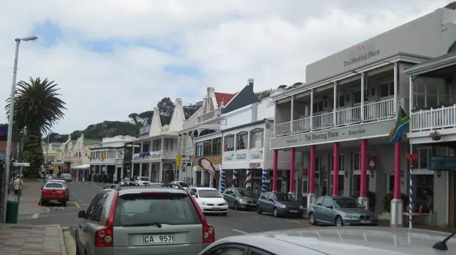 Long verandas overlook a town street lined with parked vehicles.