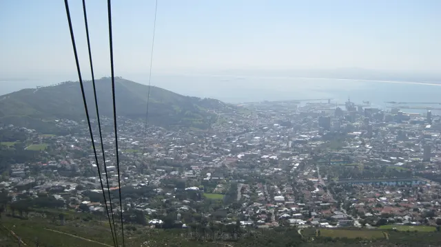 Cable lines lead toward a city spread below a rounded hill and distant sea.