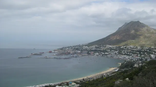 A curved beach and coastal town sit below a pointed mountain.