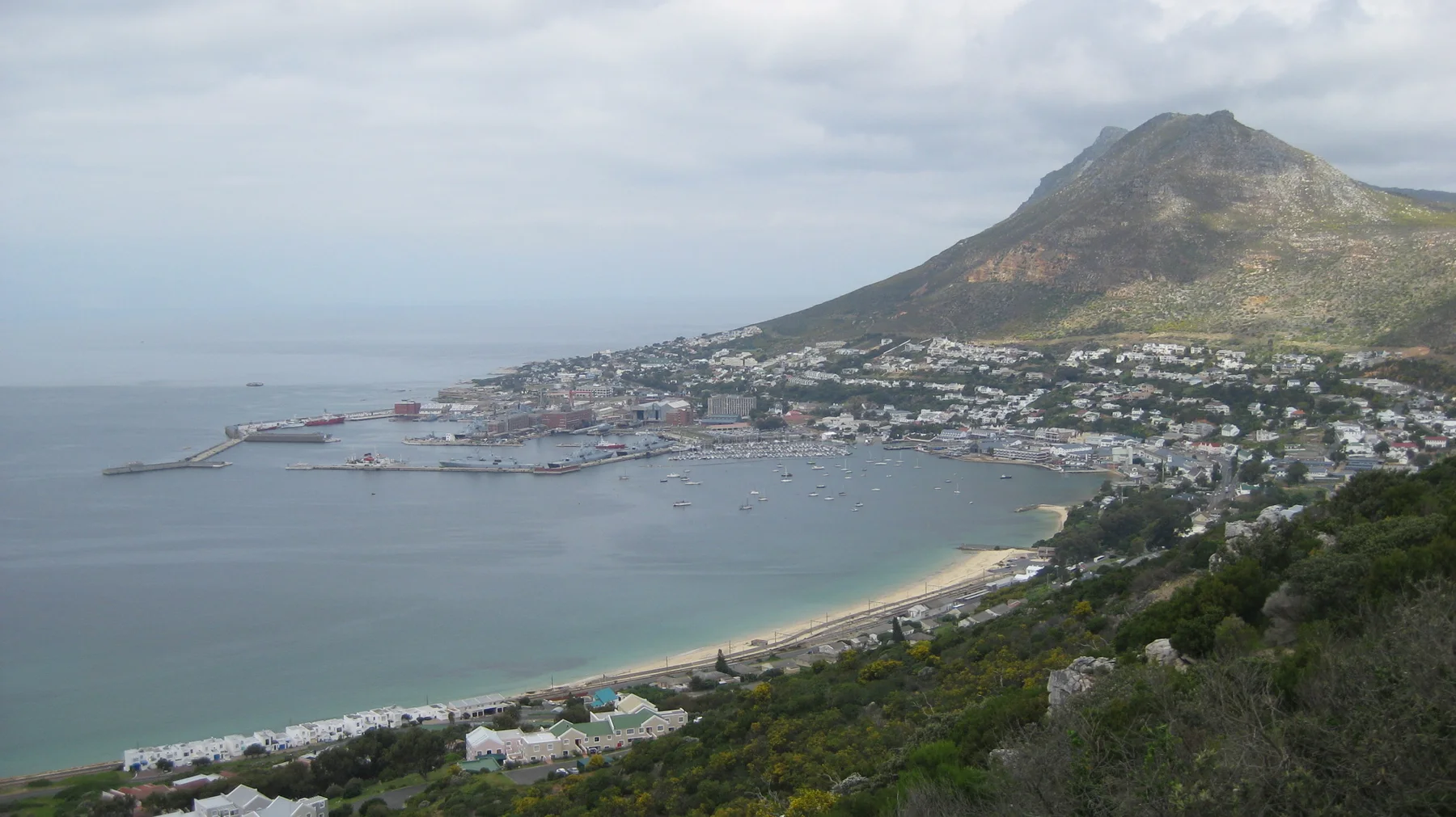 Calm coastal water curves around a town below a steep pointed mountain.