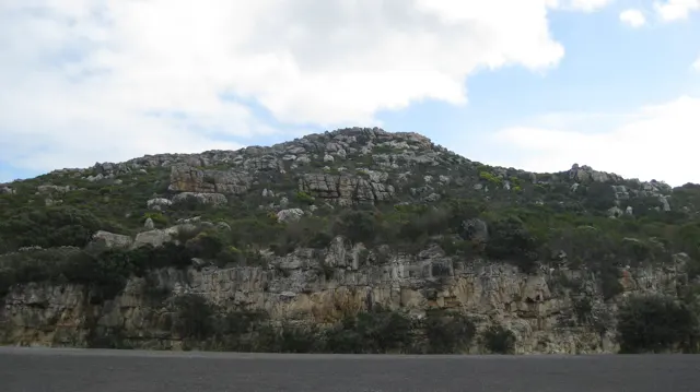 A rocky green hillside rises above the dark edge of reservoir water.