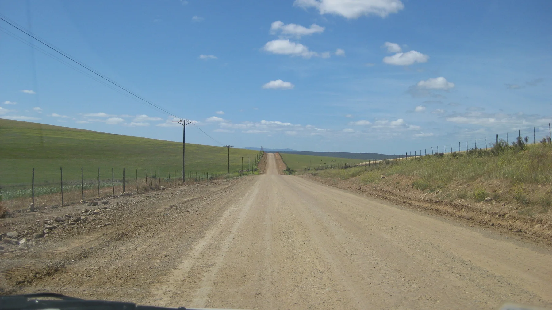 A straight dirt road follows fences and utility poles across open farmland.