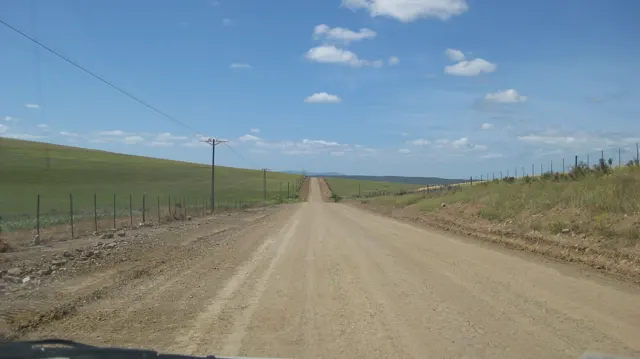 A straight dirt road follows fences and utility poles across open farmland.
