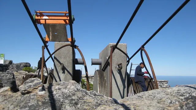 Heavy cables and metal supports cross rough summit rocks against blue sky.