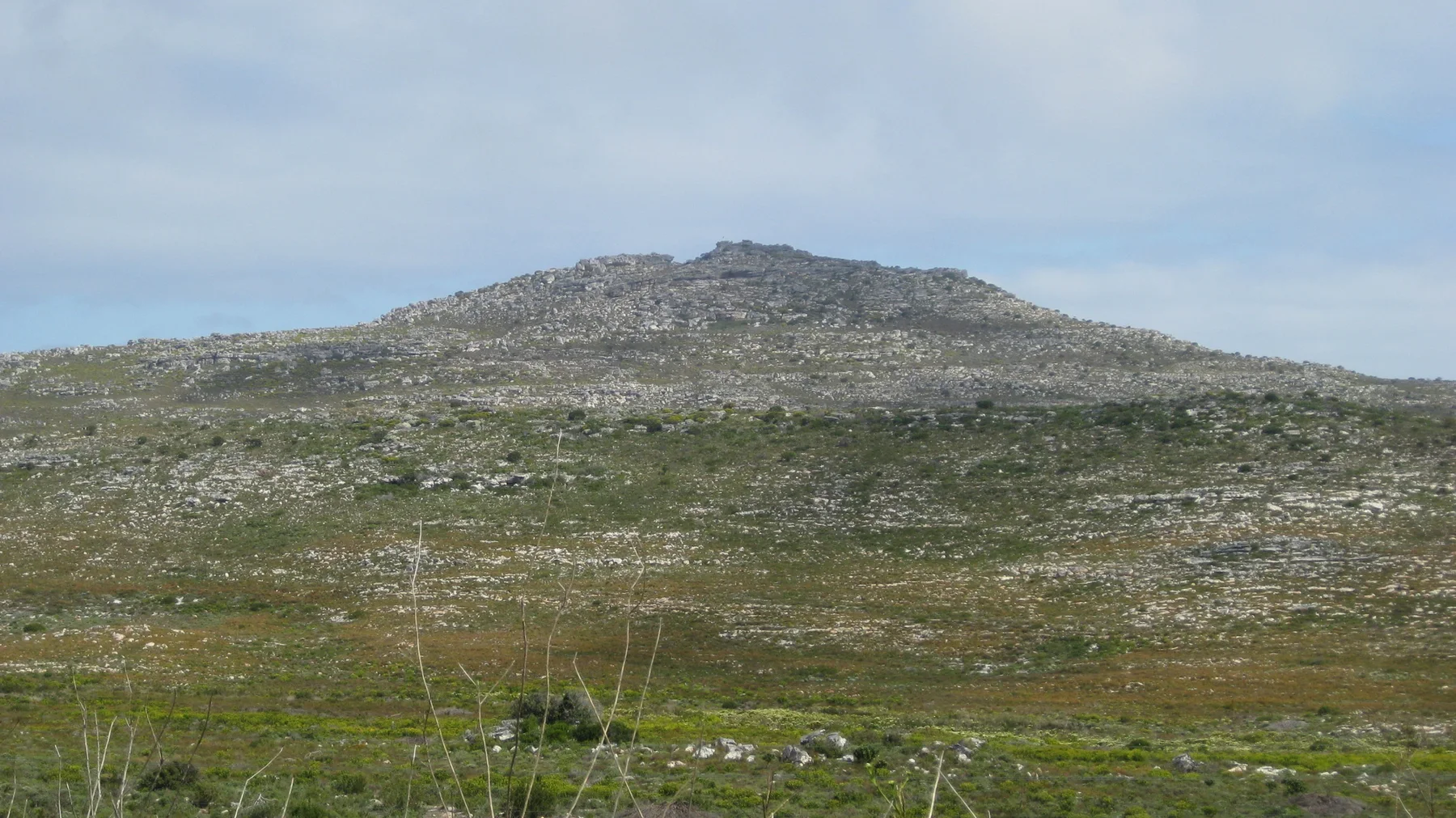 A low stony hill rises above sparse green scrub under clear sky.
