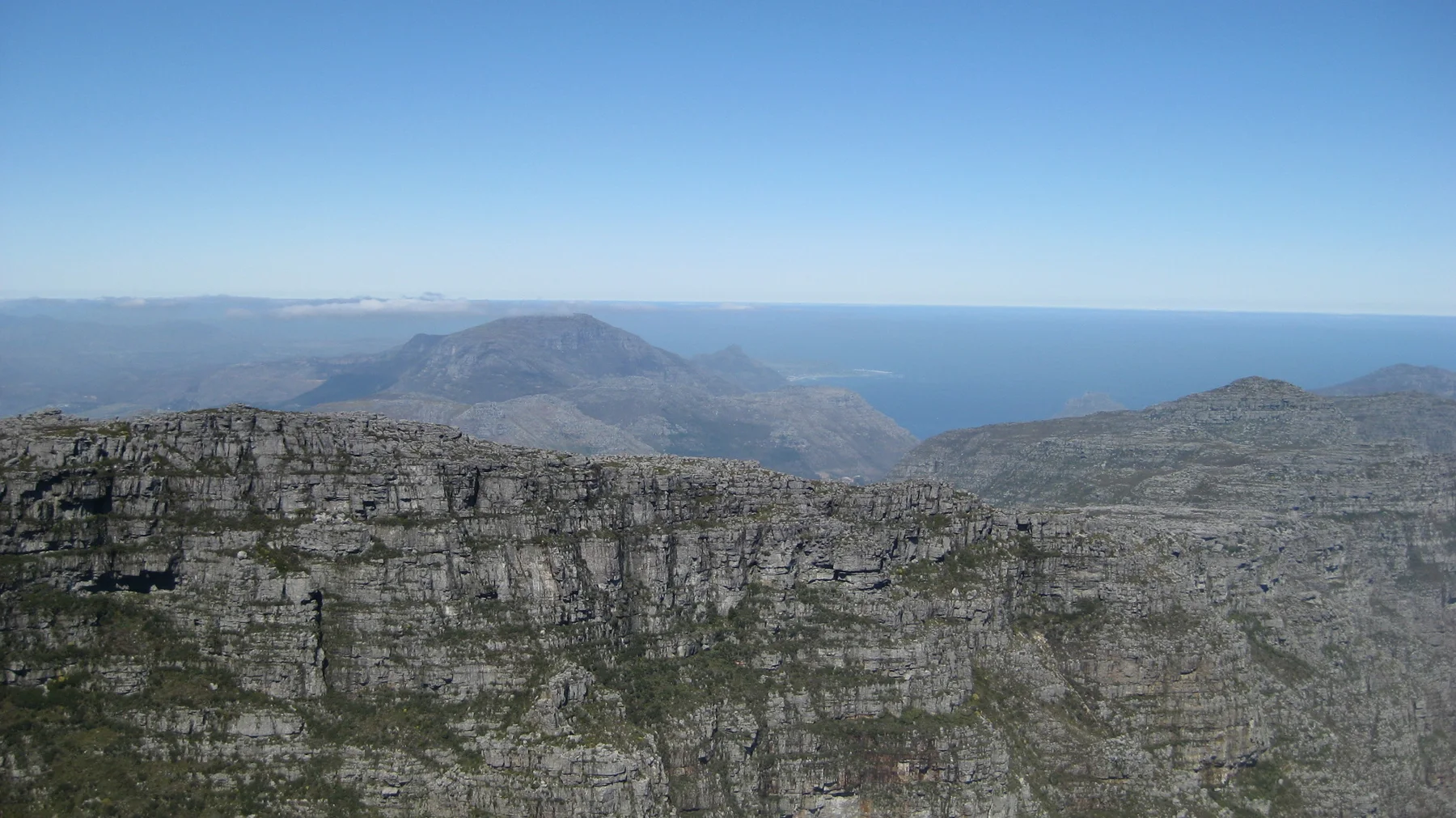 A sheer layered cliff overlooks distant ridges and a blue ocean horizon.