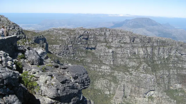 A tall layered rock wall rises beyond a rugged foreground ledge.
